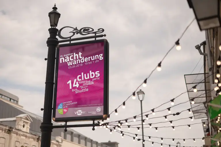 Leuchtend pinkes Veranstaltungsplakat der 19. Dresdner Nachtwanderung, montiert an einer Straßenlaterne. Ein Event-Printdesign von foxdot.me.