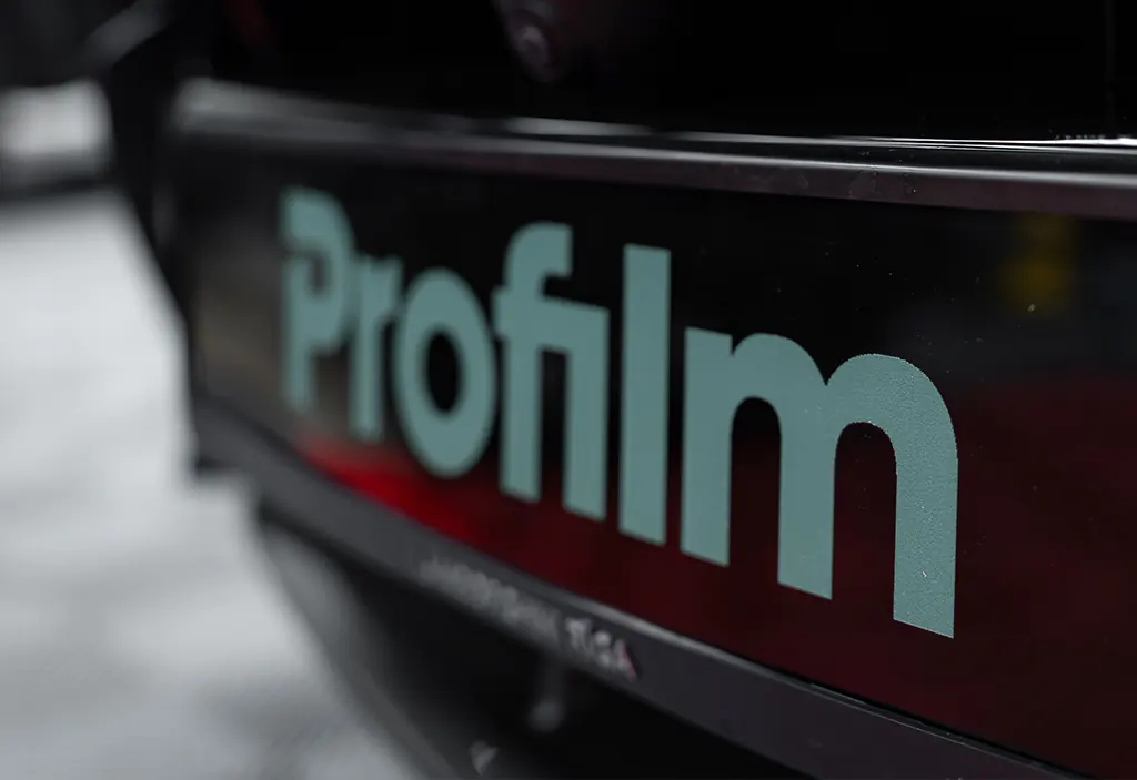 Nahaufnahme einer Fahrzeugbeschriftung mit dem matten, mintgrünen Profilm-Logo auf hochglänzendem schwarzem Untergrund. Ein Werbetechnik-Projekt von foxdot.me.